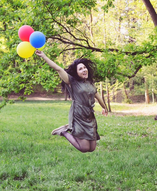 Mujer saltando con globos de colores en las manos